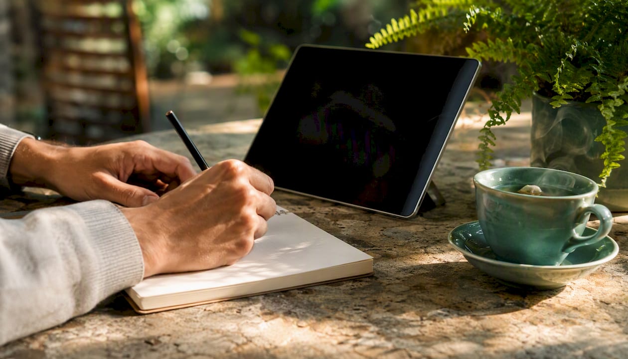 Hands taking notes near tablet and tea